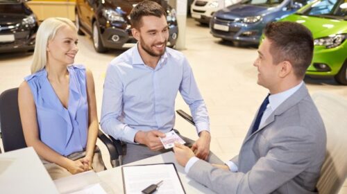 happy couple with car dealer in auto show or salon